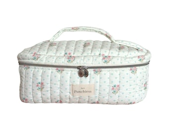 May include: A white quilted makeup bag with a floral print and a silver zipper. The bag has a handle and a label that says "Punchies" on it.