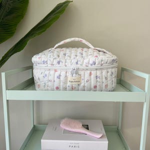 May include: White quilted makeup bag with a floral print and a zipper closure. The bag has a handle and the text "Punchless" is printed on the front.