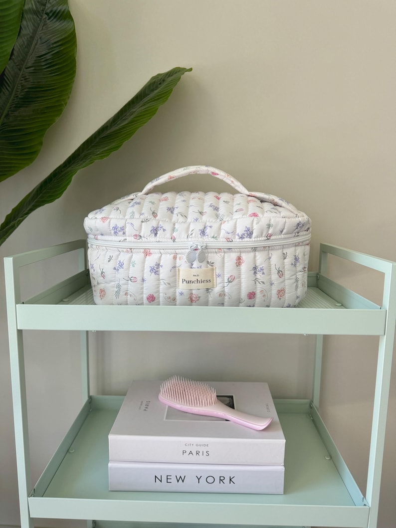 May include: White quilted makeup bag with a floral print and a zipper closure. The bag has a handle and the text "Punchless" is printed on the front.
