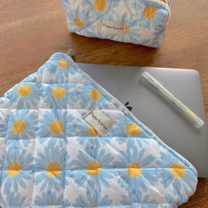 May include: Two quilted zippered pouches with a blue and yellow daisy print. The larger pouch has the text "Punchies" on it. The smaller pouch has a yellow and white gingham lining.