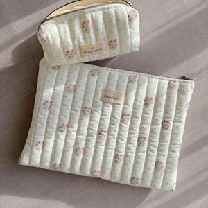 May include: Two quilted zippered pouches with a floral pattern and the word "Punchies" on each. The larger pouch is lying flat and the smaller pouch is standing upright.