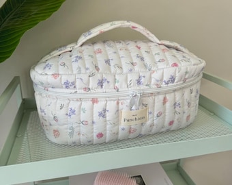 May include: White quilted oval makeup bag with a floral print and a zipper closure. The bag has a handle and a label that says "Punchiest".