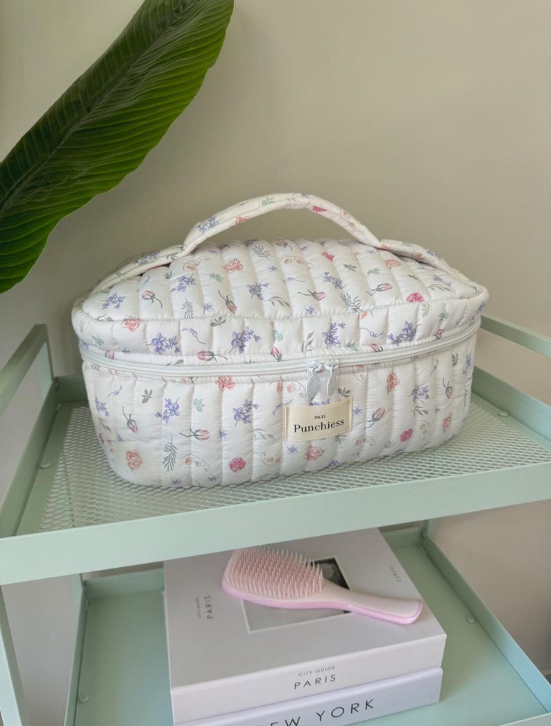 May include: White quilted oval makeup bag with a floral print and a zipper closure. The bag has a handle and a label that says "Punchiest".