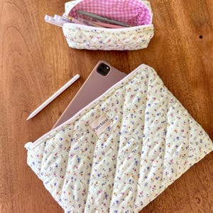 May include: A green quilted pouch with a floral pattern and the word "Punchless" printed on it. The pouch is open and a tablet computer is inside. A smaller quilted pouch with a pink and white gingham lining is also shown, filled with pens and pencils.