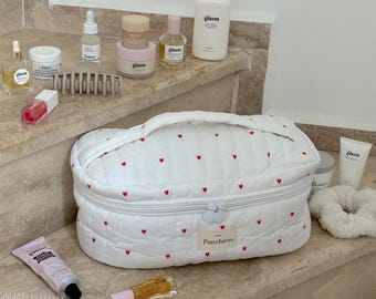 May include: A white quilted cosmetic bag with red heart embroidery, a variety of beauty products, and a pink hairbrush. The bag is labeled "Punchiess". Other products include bottles, jars, and tubes.