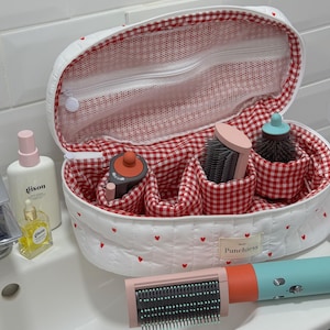 May include: A white quilted cosmetic bag with red heart accents and a red and white gingham interior. The bag contains various beauty tools, including brushes and a hair dryer. The text "Punchiess" is visible on the bag.