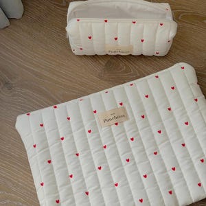 May include: Two white quilted cosmetic bags with red heart patterns. One is a rectangular pouch with a zipper, and the other is a larger, flat case. Both have a small label that reads "Punchiess".