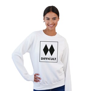 May include: White sweatshirt with a black graphic of two overlapping diamonds inside a square with the word "DIFFICULT" underneath.