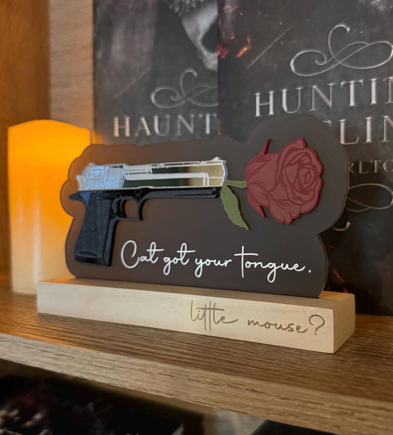 May include: A wooden sign with a black gun and a red rose, with the text "Cat got your tongue. little mouse?"