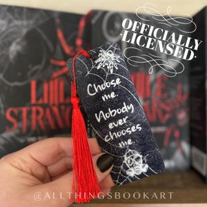May include: Black and white bookmark with a spider web design and the text "Choose me. Nobody ever chooses me." The bookmark has a red tassel.