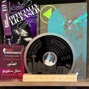 May include: A collection of music-themed memorabilia, including a clear disc with the text "R3V3RB supernova 11:11" and a cityscape design. A purple VIP lanyard and a concert pass are also visible.