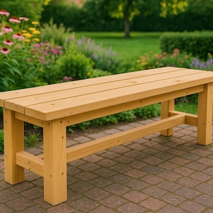 Op de afbeelding: Een lichtgekleurde houten bank met een rechthoekige zitting en vier stevige poten. De bank is gemaakt van planken en staat op een stenen terras, met een tuin en bloemen op de achtergrond.