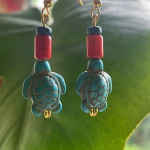 May include: A pair of gold dangle earrings with turquoise turtle charms, red and blue beads, and gold hooks.