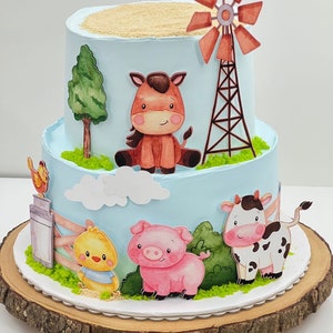 Könnte beinhalten: Eine zweistöckige Torte, die mit einem Bauernhof-Thema verziert ist. Die Torte ist mit einer Windmühle, einem Pferd, einer Kuh, einem Schwein und einem Küken verziert. Die Torte steht auf einem Holzkuchenständer.