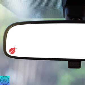 May include: A red ladybug sticker on a rearview mirror in a car.