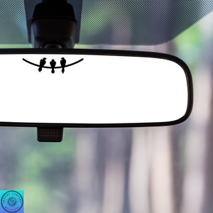 May include: A rearview mirror with a black silhouette of three birds perched on a branch. The birds are facing to the right.