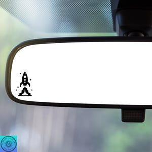 May include: A black and white rocket ship decal with stars, perfect for a car rearview mirror.
