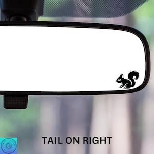 May include: A black silhouette of a squirrel is on the rearview mirror of a car. The text "TAIL ON RIGHT" is below the mirror.