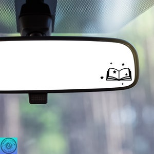 May include: A black and white car rearview mirror with a sticker of an open book with stars above it.