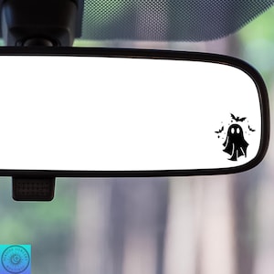 May include: A black and white ghost with a friendly face is shown in a rearview mirror. The ghost is surrounded by bats and stars.