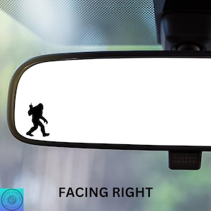 May include: A black silhouette of a Bigfoot figure giving the middle finger, placed on a rearview mirror of a car. The text "FACING RIGHT" is below the mirror.