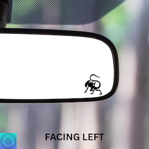 May include: A black vinyl decal of a stylized creature, facing left, is affixed to a car's rearview mirror. The text "FACING LEFT" is printed in white below the mirror. The decal is a unique car accessory.