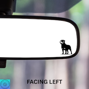 May include: A black Rottweiler dog silhouette decal applied to the surface of a vehicle rearview mirror. The dog is depicted in a standing profile position facing toward the left side of the mirror. The text FACING LEFT is visible below.