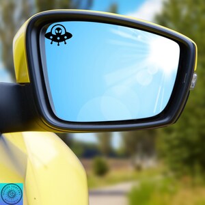 Peut inclure: Une voiture jaune avec un r&eacute;troviseur lat&eacute;ral noir. Le r&eacute;troviseur refl&egrave;te un ciel bleu avec des nuages blancs. Un autocollant de vaisseau spatial extraterrestre noir est sur le r&eacute;troviseur.