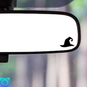 May include: A black witch hat silhouette sticker on a rearview mirror of a car.