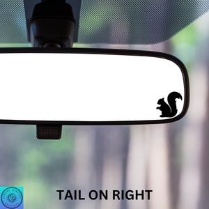 May include: A black silhouette of a squirrel with its tail facing right is on a rearview mirror of a car. The text "TAIL ON RIGHT" is below the mirror.