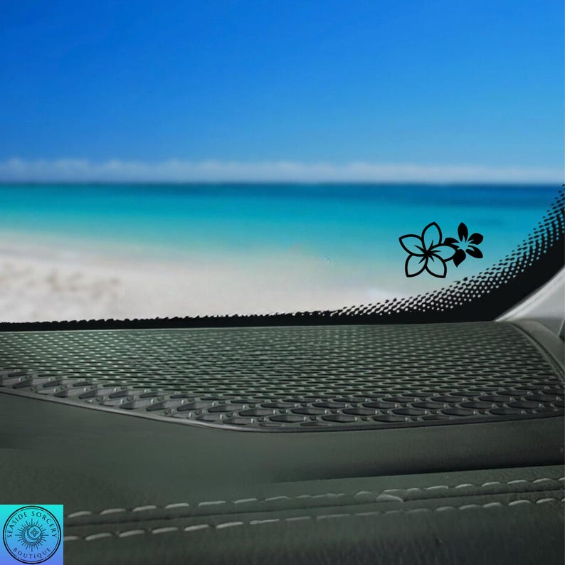 Pu&ograve; includere: Un adesivo floreale nero &egrave; applicato al finestrino di un'auto, con una scena di spiaggia e oceano sullo sfondo. L'adesivo presenta due fiori stilizzati. Il cruscotto dell'auto &egrave; visibile in primo piano, con una superficie strutturata e cuciture bianche.