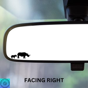 May include: A black and white silhouette of a rhinoceros and a baby rhinoceros facing right on a white car rearview mirror. The text "FACING RIGHT" is below the mirror.