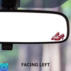 May include: A rearview mirror with a red glitter ruby slipper sticker on the glass. The sticker is facing left. The text "FACING LEFT" is printed below the mirror.