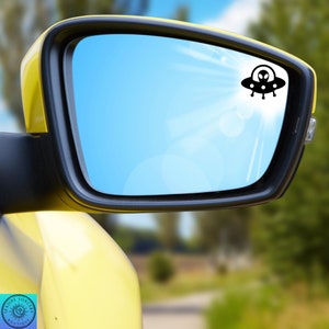 Peut inclure: Une voiture jaune avec un r&eacute;troviseur bleu. Un autocollant de vaisseau spatial extraterrestre noir est sur le miroir.
