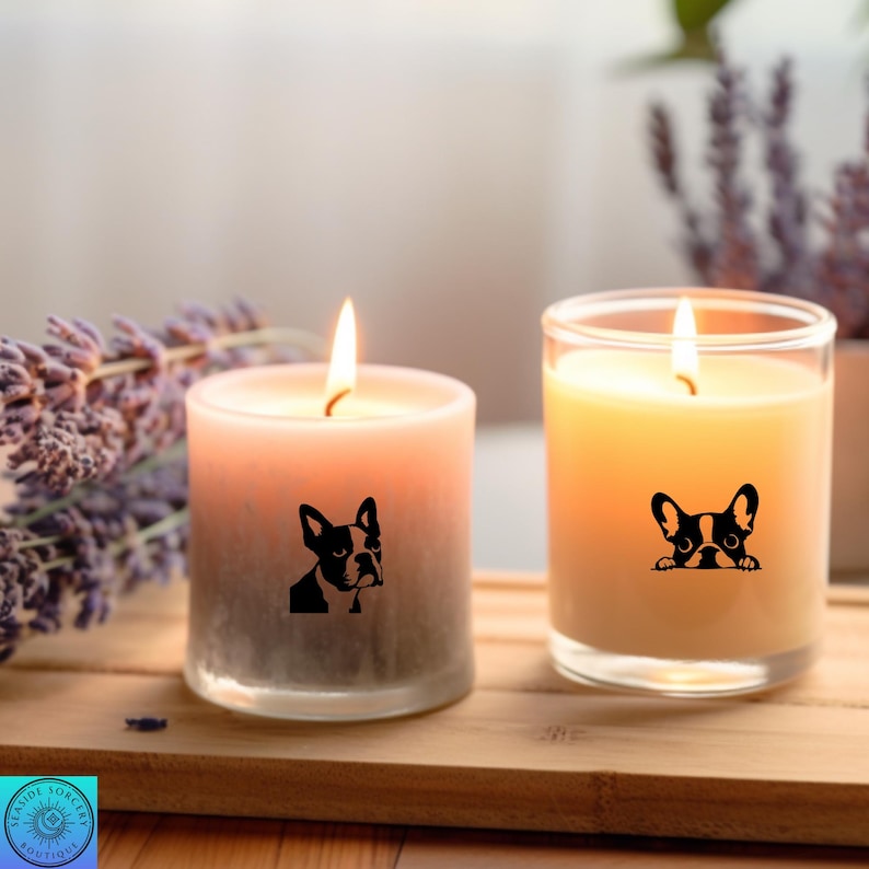 May include: Two lit candles with a dog graphic. One candle is a gradient of pink to gray, the other is yellow. Both candles have a black and white French Bulldog design. The candles are on a wooden tray.