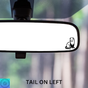 May include: A black and white silhouette of a ferret sitting on a rearview mirror in a car. The text "TAIL ON LEFT" is visible below the mirror.
