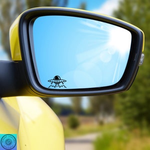 May include: A black and white UFO sticker on a blue car side mirror. The sticker is of a flying saucer with a dome and a beam of light coming out of the bottom.