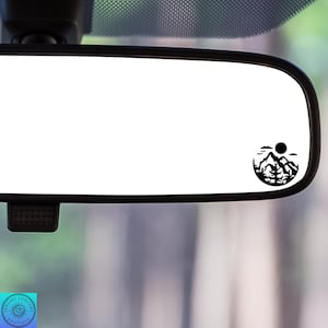 May include: A black and white silhouette of a mountain range with a sun and clouds in a circle. The image is on a white background and is a car mirror sticker.