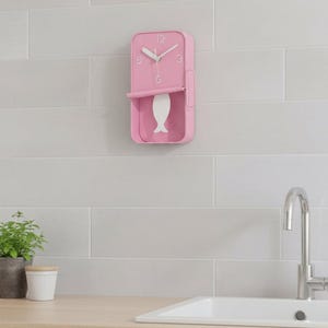 May include: A rectangular pink wall clock with rounded corners, featuring white hour markers at 12, 3, 6, and 9. The clock face includes white hour and minute hands and a white pendulum shaped like a fish that hangs below the main clock housing.