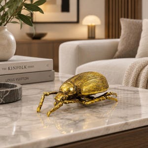 May include: A decorative beetle figurine crafted with a metallic gold finish, featuring a textured, ribbed wing casing and articulated legs. The insect sculpture displays a realistic anatomical form with a smooth head and detailed segments.