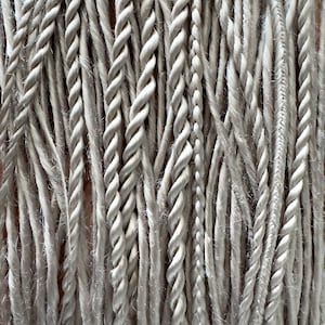 May include: A close-up of a bundle of white and grey braided cords. The cords are arranged in a vertical pattern, creating a textured background.