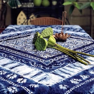May include: A blue and white patterned tablecloth with a diamond design. Green lotus seed pods and a wooden incense holder with incense sticks are arranged on the table. The tablecloth has a tie-dye effect.
