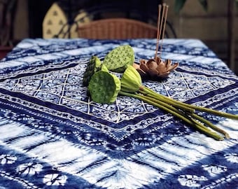 May include: A blue and white patterned tablecloth with a diamond design. Green lotus seed pods and a wooden incense holder with incense sticks are arranged on the table. The tablecloth has a tie-dye effect.