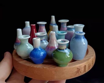 May include: A collection of miniature ceramic vases in various colours and designs, displayed on a wooden base. The vases are arranged in a circle, with the base in the centre. The base is inscribed with the word "XINYU".