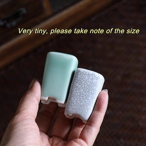 Op de afbeelding: Twee kleine keramische containers. Eén is lichtgroen, de andere is wit met een craquelé-patroon. De tekst "Very tiny, please take note of the size" staat in het geel boven de containers.