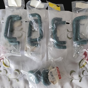 Può includere: Diversi morsetti a C nuovi, color verde acqua, sono confezionati in plastica trasparente. I morsetti hanno una finitura strutturata e sono esposti su una tovaglia bianca ricamata. Una piccola etichetta è visibile.