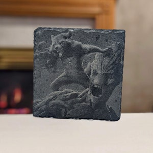 May include: A black slate coaster with a laser-etched image of Rocket Raccoon and Groot from Guardians of the Galaxy. The image is in grayscale and shows Rocket with his arms outstretched and Groot with his mouth open.