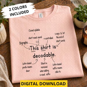 May include: A light pink t-shirt featuring black text that reads: This shirt is decodable. The design includes arrows pointing to various linguistic terms such as Closed syllable, Digraphs, r-controlled, s says /z/, Latin-based prefix, Silent-e, and Latin-based suffix.