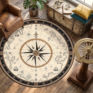 Op de afbeelding: Een ronde beige vloerkleed met een kompasroosontwerp. Het vloerkleed heeft een zwarte rand met gradenmarkeringen en nautische illustraties. De kompasroos staat centraal, met de windrichtingen aangegeven. Decoratief en functioneel.