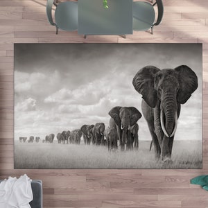 May include: A black and white photograph of a herd of elephants walking across a grassy plain. The elephants are in a single file line, with the largest elephant in the front. The sky is cloudy and the grass is tall.